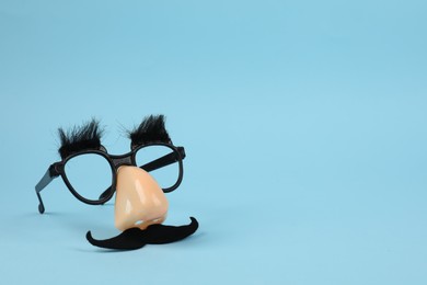 Photo of Funny mask with fake mustache, nose and glasses on light blue background. Space for text