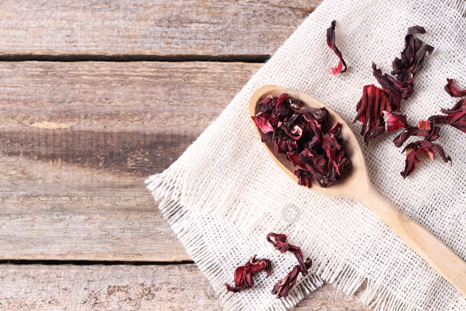 Photo of Spoon with dry hibiscus tea on wooden table, flat lay. Space for text