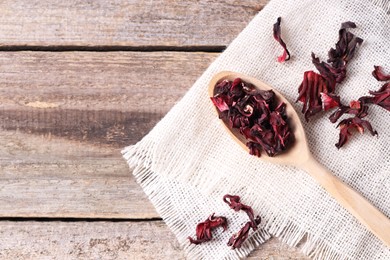 Photo of Spoon with dry hibiscus tea on wooden table, flat lay. Space for text