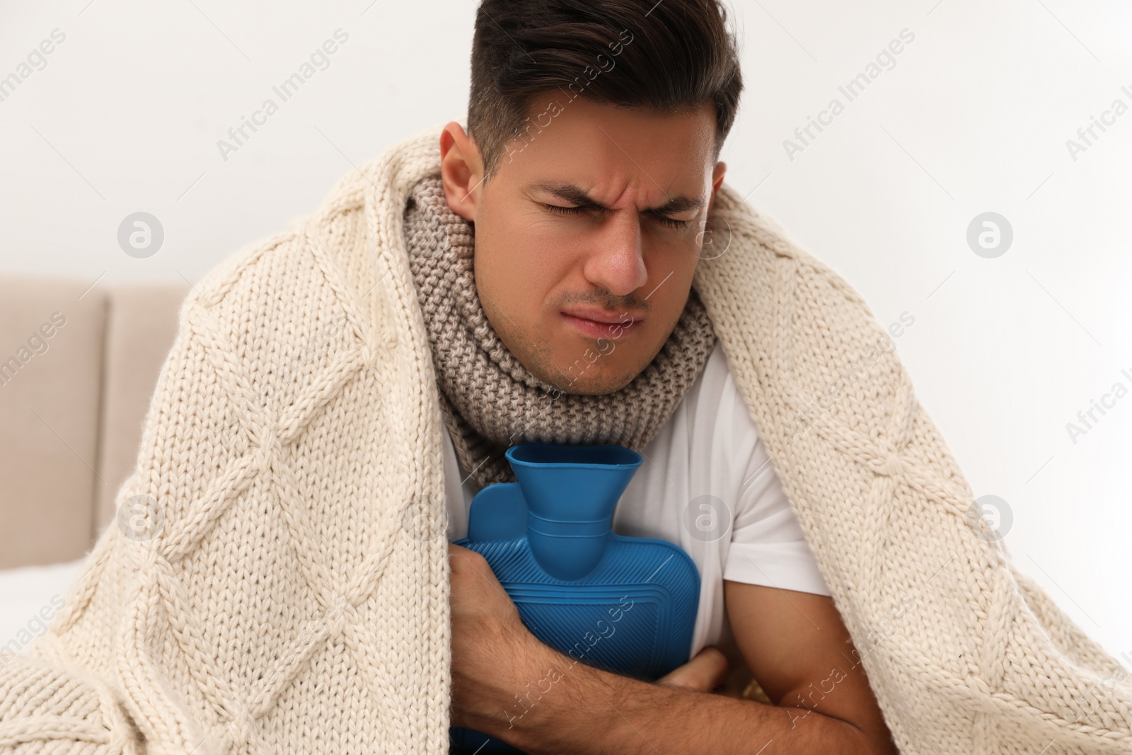 Photo of Ill man with hot water bottle suffering from cold at home