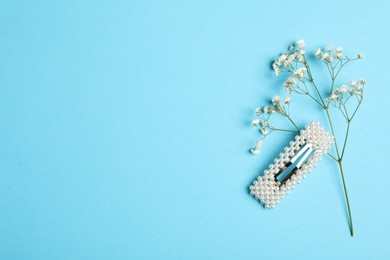 Stylish hair clip and flowers on light blue background, flat lay. Space for text