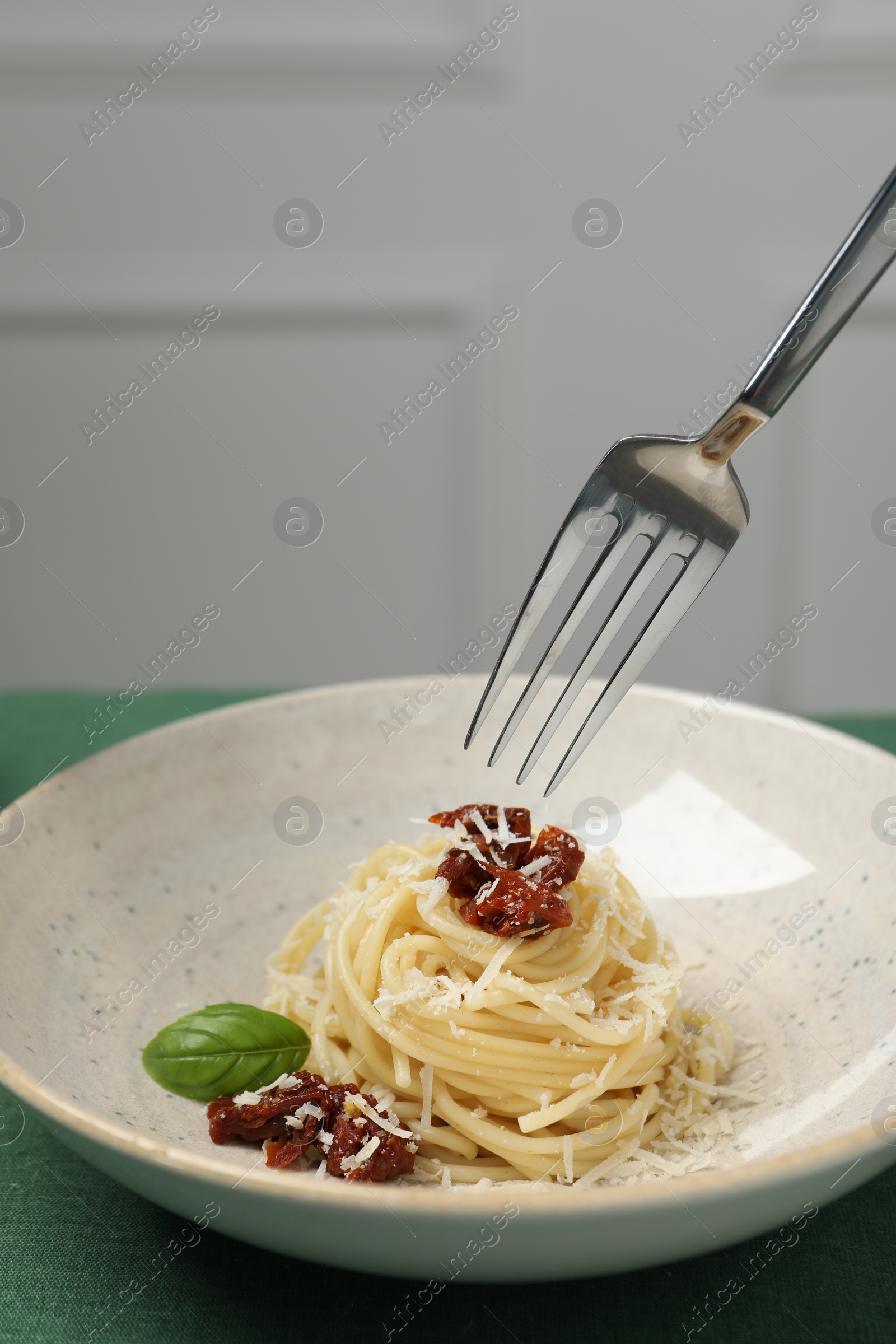 Photo of Eating tasty spaghetti with sun-dried tomatoes and cheese from plate at table, closeup. Exquisite presentation of pasta dish