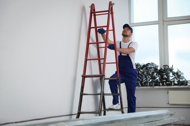 Construction worker climbing up stepladder in room prepared for renovation