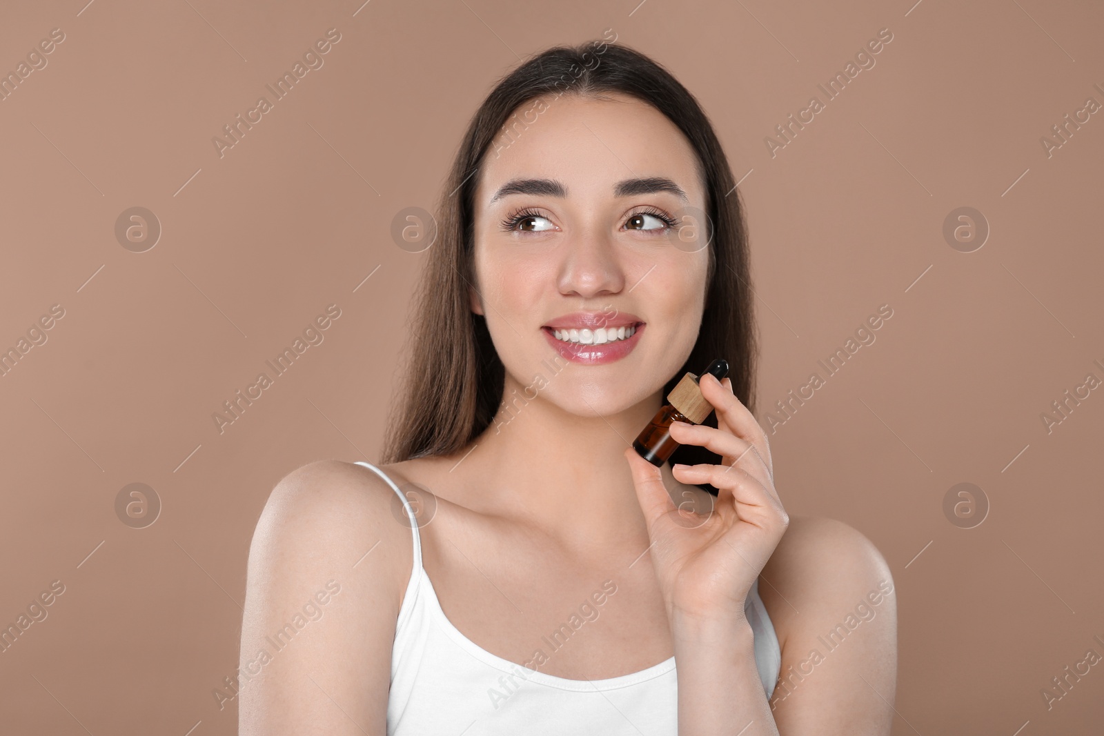 Photo of Beautiful young woman with bottle of essential oil on brown background