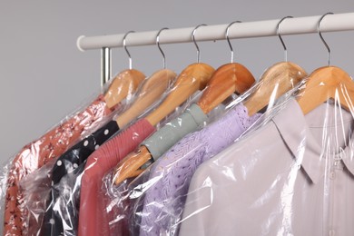 Photo of Dry-cleaning service. Many different clothes in plastic bags hanging on rack against grey background, closeup