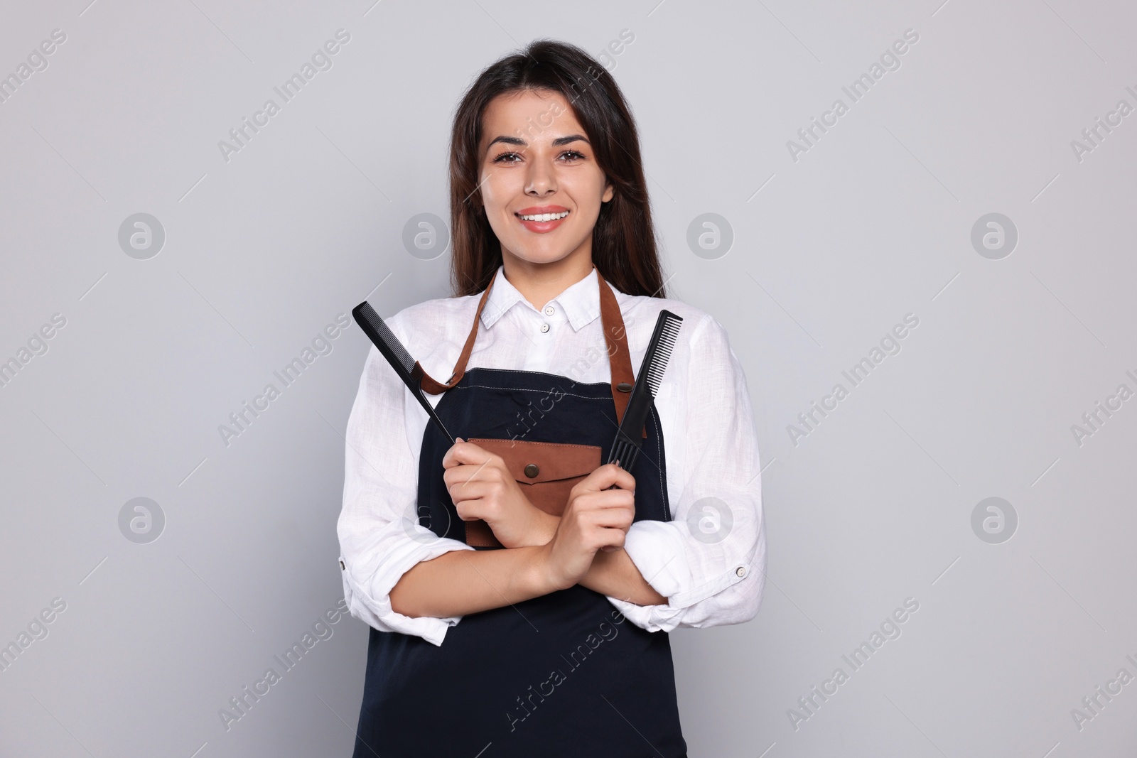 Photo of Portrait of happy hairdresser with professional combs against light grey background