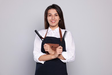 Portrait of happy hairdresser with professional combs against light grey background