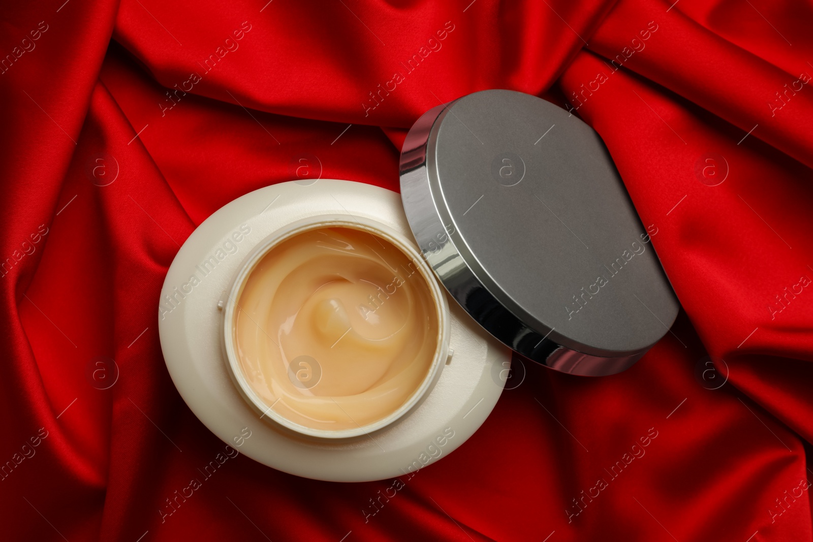 Photo of Open jar of hair care cosmetic product on red fabric, top view