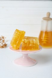 Photo of Stand with natural honeycombs and honey on white table, selective focus. Space for text