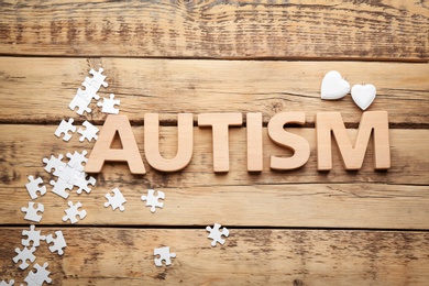 Word "Autism" and puzzle pieces on wooden background