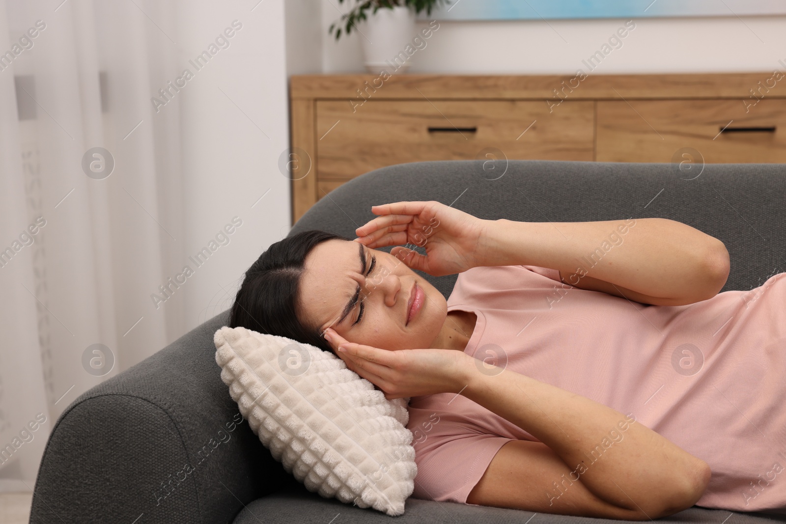 Photo of Sad woman suffering from headache on sofa indoors