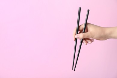 Photo of Woman holding pair of black chopsticks on pink background, closeup. Space for text