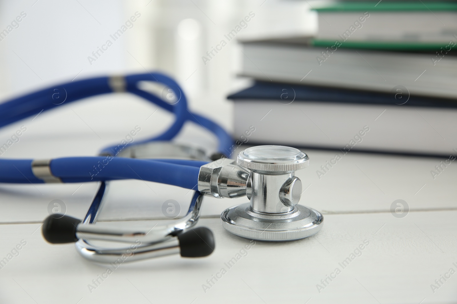 Photo of One new medical stethoscope and books on white table, closeup