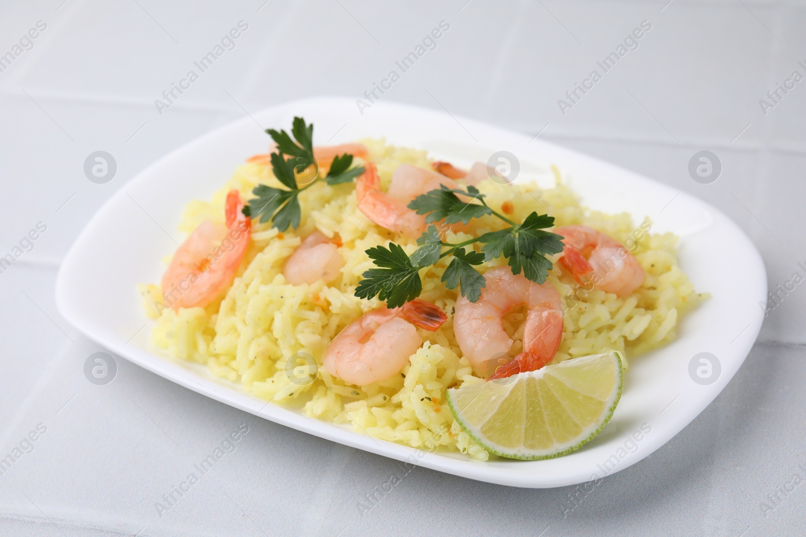 Photo of Delicious risotto with shrimps, lime and parsley on white tiled table, closeup