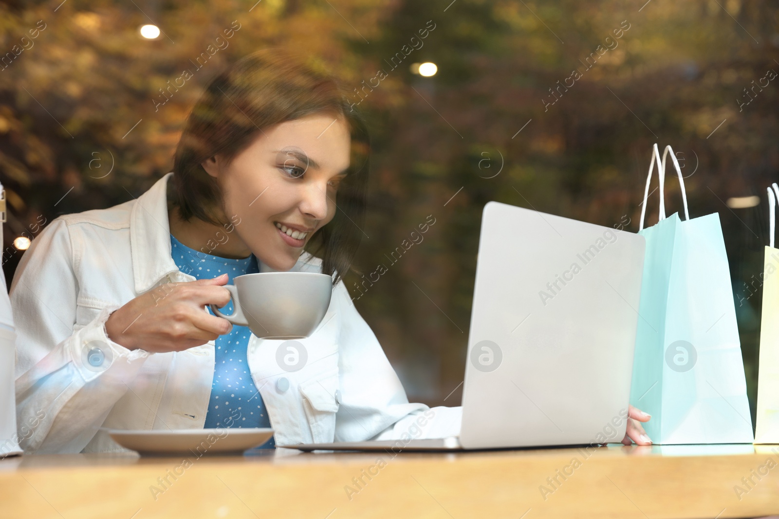 Photo of Special Promotion. Happy young woman with cup of drink using laptop in cafe, view from outdoors