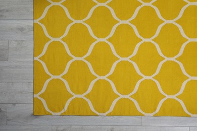 Yellow carpet with geometric pattern on wooden floor, top view