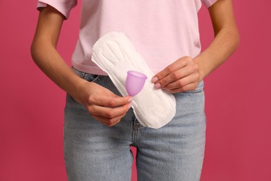 Photo of Young woman with menstrual cup and pad on bright pink background, closeup