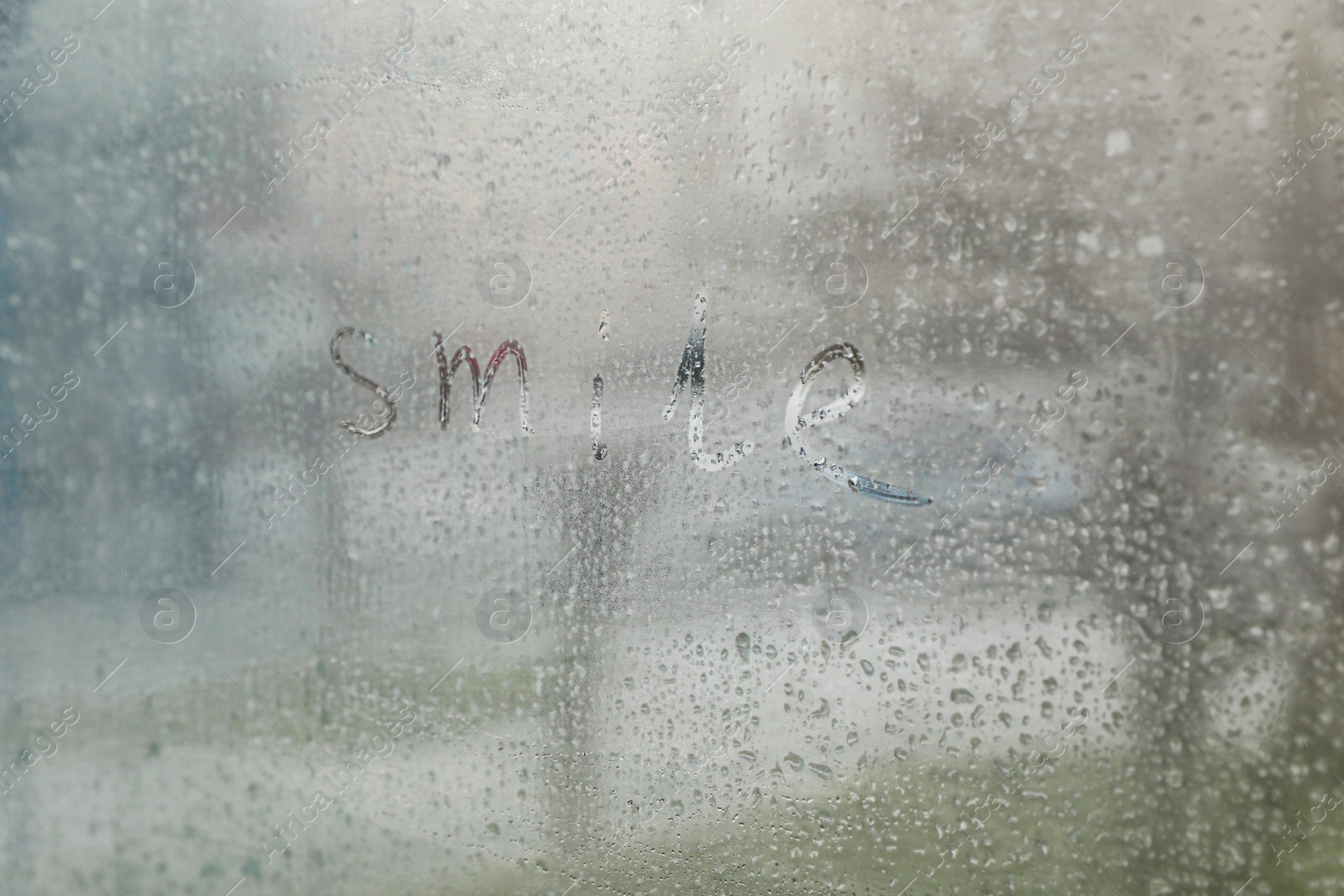 Photo of Word Smile written on foggy window. Rainy weather