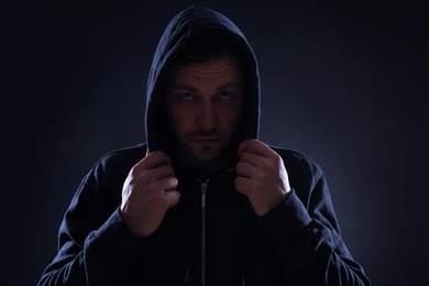 Mysterious man in hoodie on dark background. Dangerous criminal