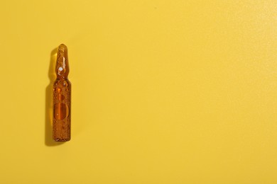 Photo of Glass ampoule with liquid on yellow background, top view. Space for text