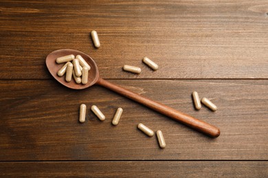 Dietary supplement capsules with spoon on wooden table, flat lay