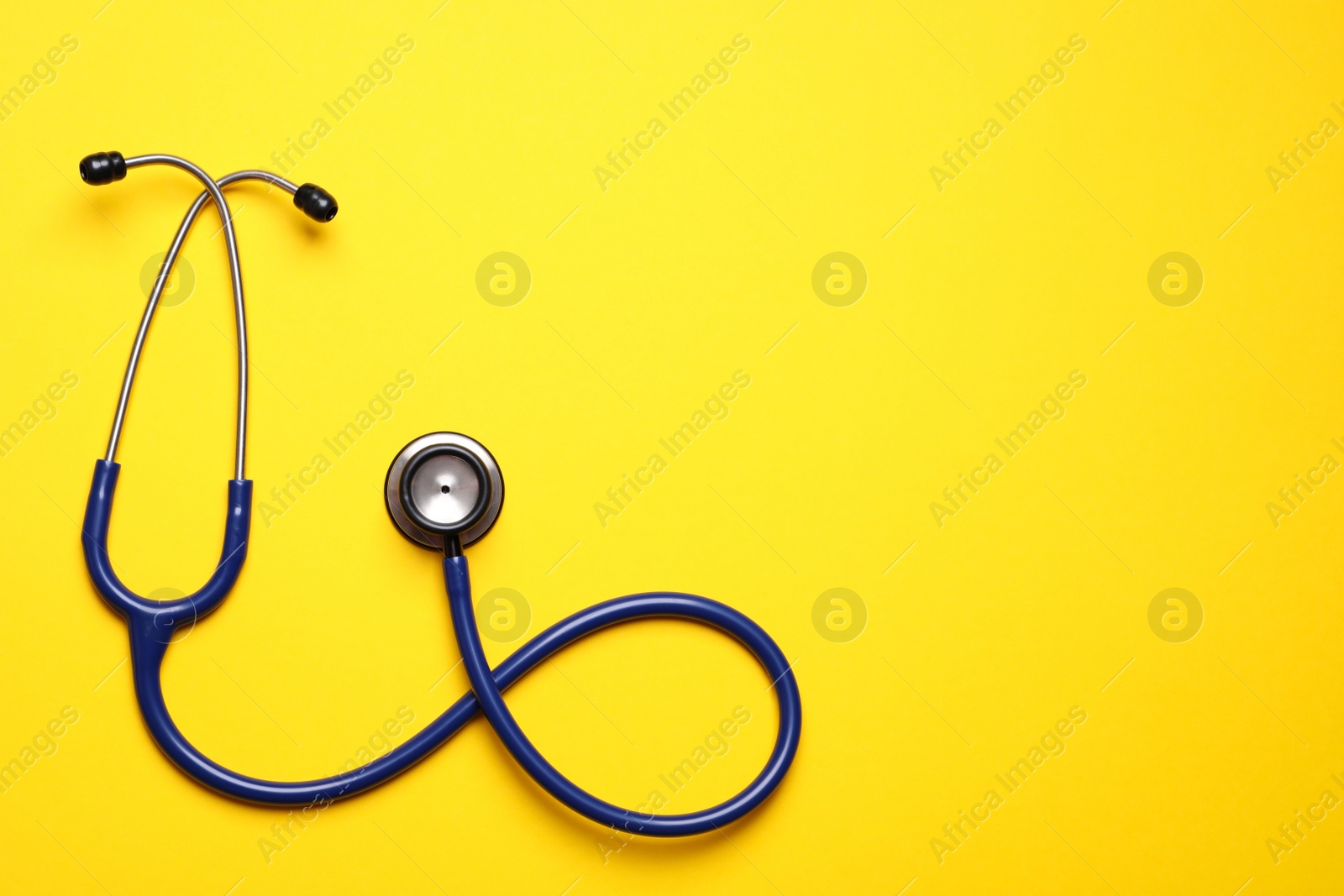 Photo of Stethoscope on yellow background, top view. Space for text