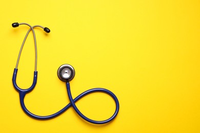 Stethoscope on yellow background, top view. Space for text