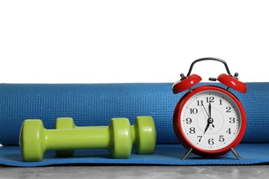 Photo of Alarm clock, yoga mat and dumbbells on grey marble table. Morning exercise