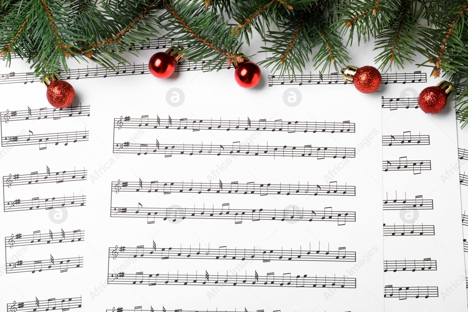 Photo of Fir tree branches and red balls on Christmas music sheets with notes, flat lay