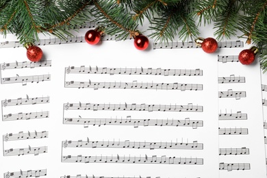 Photo of Fir tree branches and red balls on Christmas music sheets with notes, flat lay