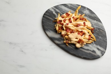 Photo of Delicious French fries with bacon and cheese sauce on white marble table, top view. Space for text