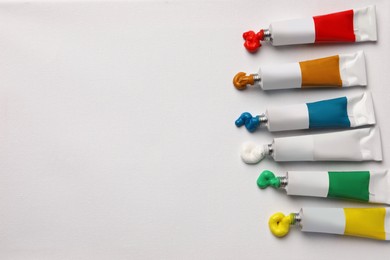 Photo of Tubes with oil paints on white canvas, flat lay. Space for text