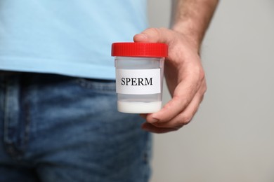 Photo of Donor holding container with sperm on beige background, closeup