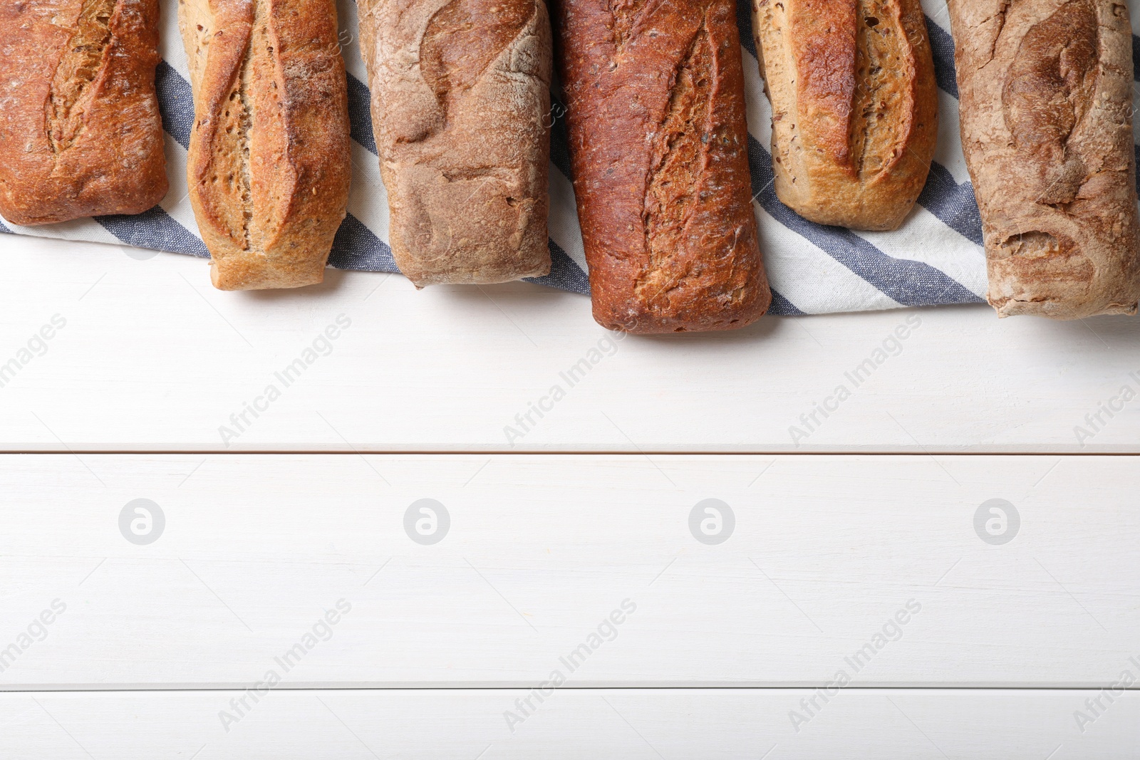 Photo of Different tasty baguettes on white wooden table, flat lay. Space for text