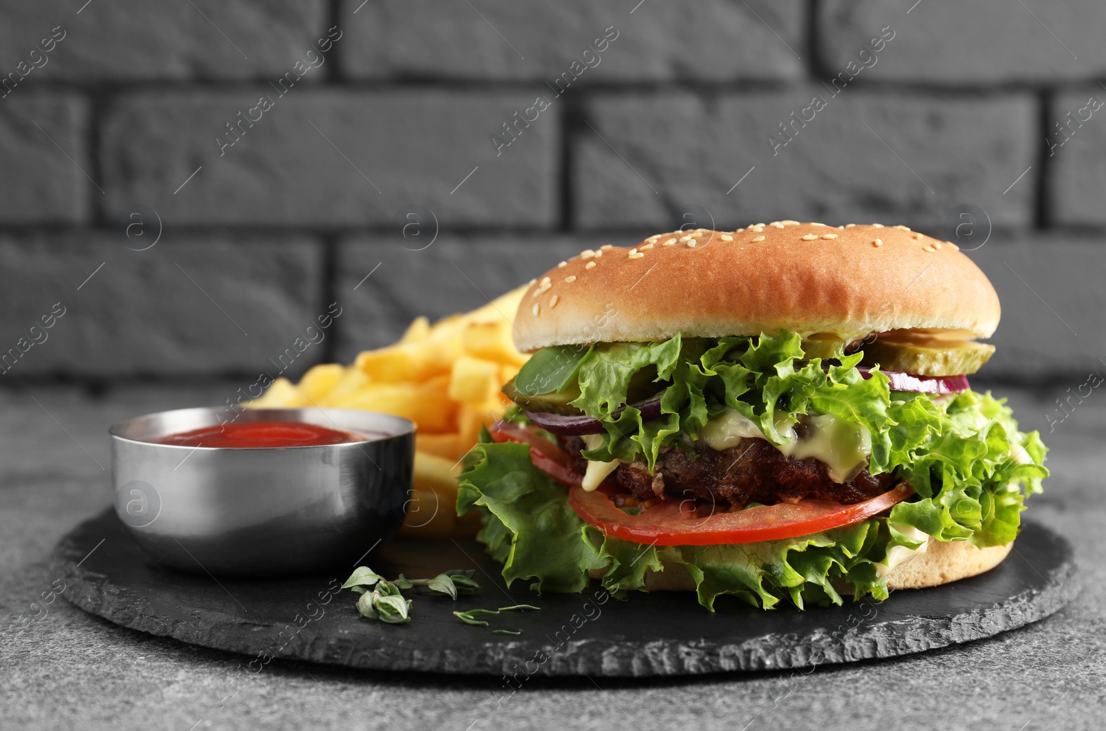 Photo of Delicious burger with beef patty, tomato sauce and french fries on grey table