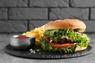 Delicious burger with beef patty, tomato sauce and french fries on grey table