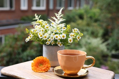 Photo of Cup of delicious chamomile tea and fresh flowers outdoors on sunny day