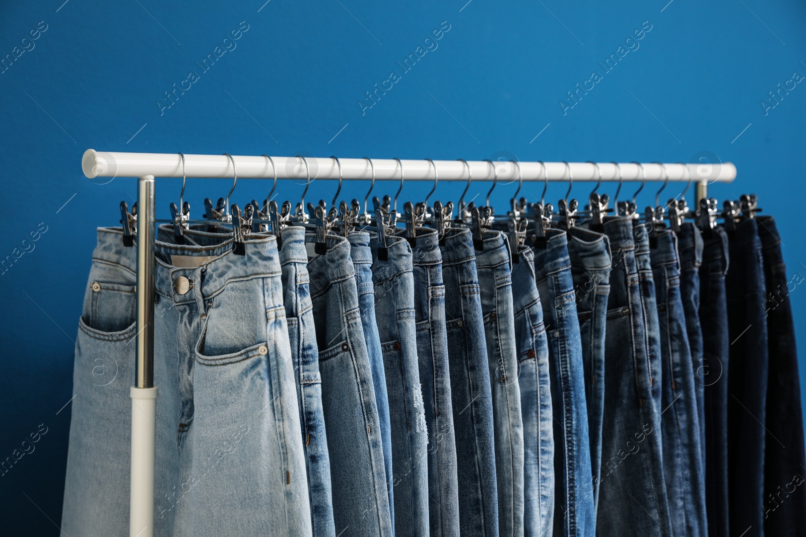 Photo of Rack with stylish jeans on blue background, closeup