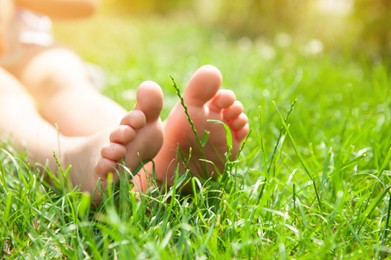 Child sitting barefoot on green grass outdoors, closeup