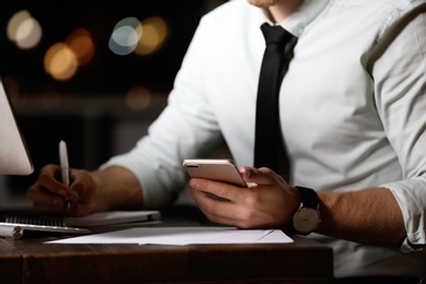 Young man with mobile phone working in office at night, closeup