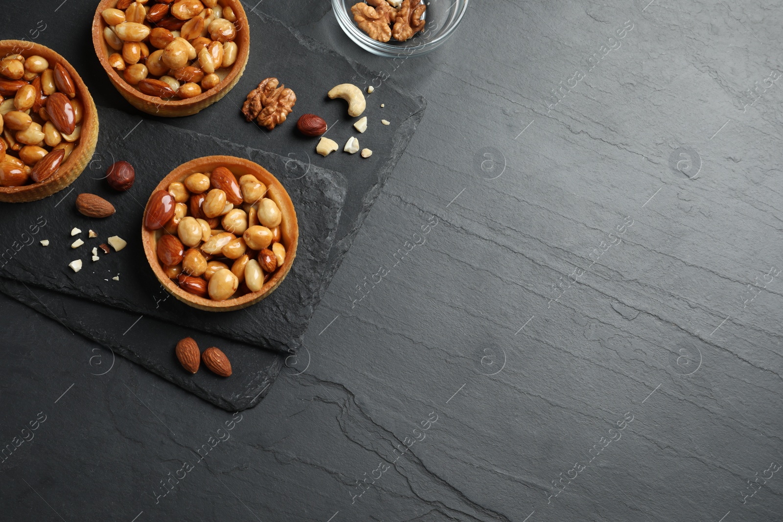 Photo of Tartlets with caramelized nuts on black table, top view and space for text. Delicious dessert