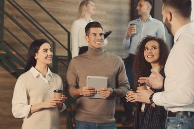 Photo of Group of coworkers talking during coffee break on stairs in office