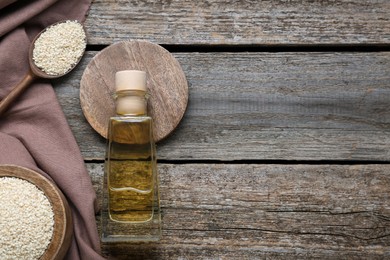 Bottle of organic sesame oil and seeds on wooden table, flat lay. Space for text