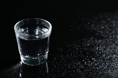 Photo of Glass of vodka on black wet table, space for text