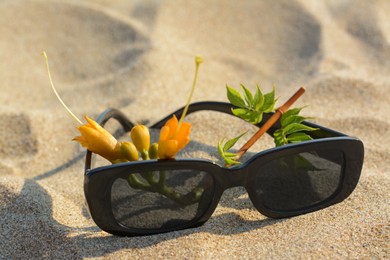Stylish sunglasses and tropical flower on sand, closeup