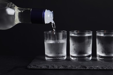Photo of Pouring vodka from bottle in glass on black table