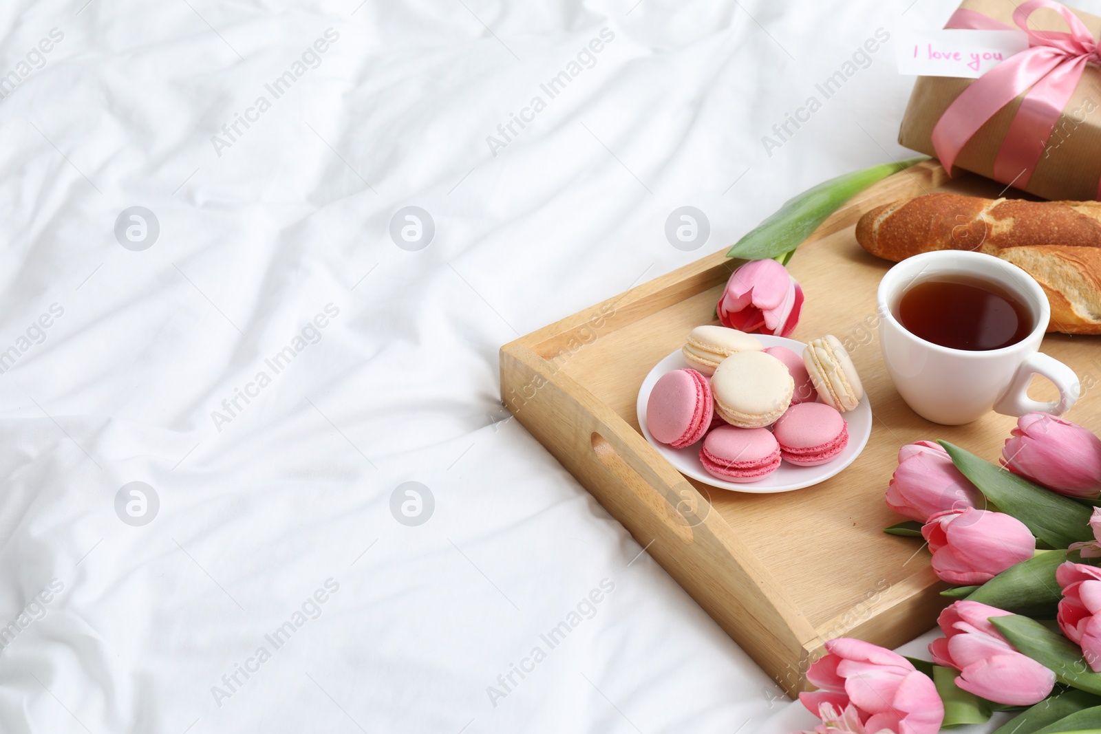 Photo of Delicious breakfast, flowers, gift box and card with phrase I Love You on bed, space for text