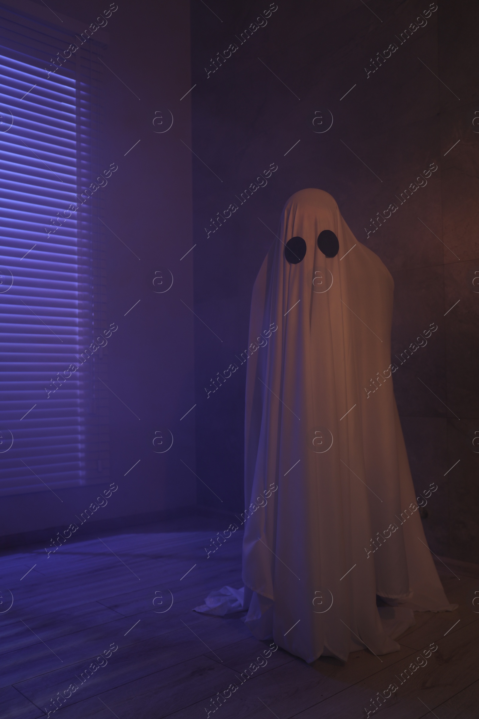 Photo of Creepy ghost. Woman covered with sheet in color lights