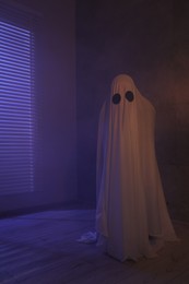 Photo of Creepy ghost. Woman covered with sheet in color lights