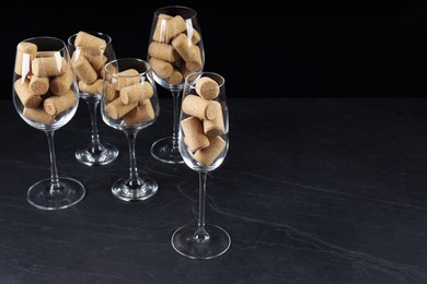 Photo of Glasses full of wine corks on black table. Space for text
